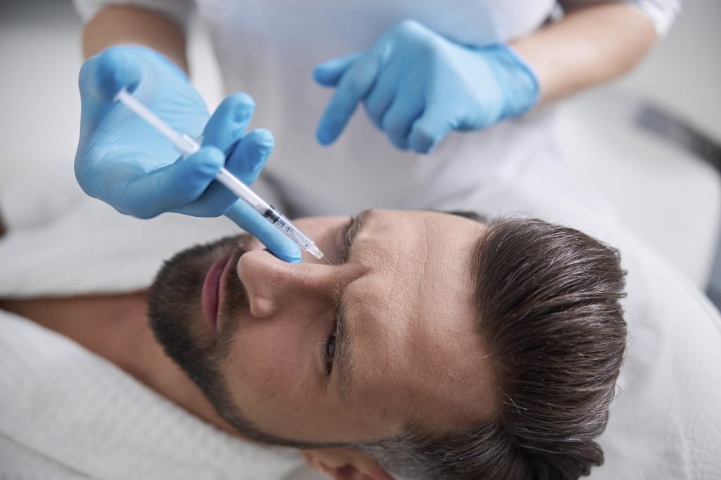 Man grimaces of pain while skilled cosmetologist does injection of lifting filler
